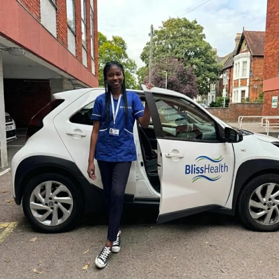 A BlissHealth carer beside a plain white car displaying the BlissHealth name and logo